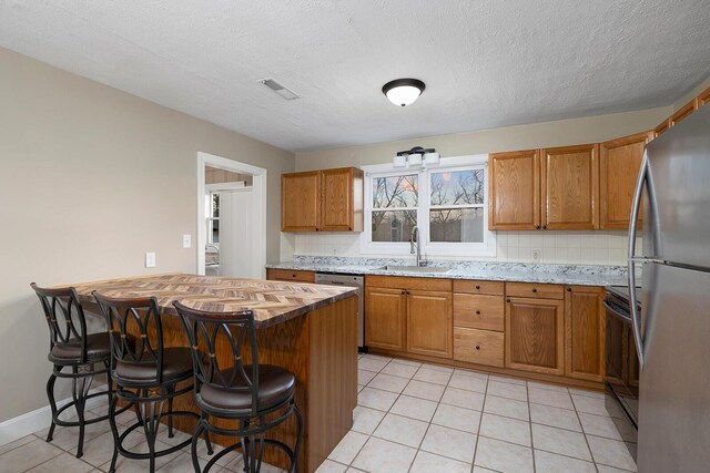 621 S Woodhaven Rd, Nixa, MO 65714 - kitchen with stainless steel appliances, a breakfast bar, brown cabinetry, light tile patterned floors, and a textured ceiling