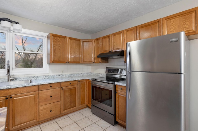 621 S Woodhaven Rd, Nixa, MO 65714 - kitchen with appliances with stainless steel finishes, under cabinet range hood, light tile patterned flooring, brown cabinetry, and a textured ceiling