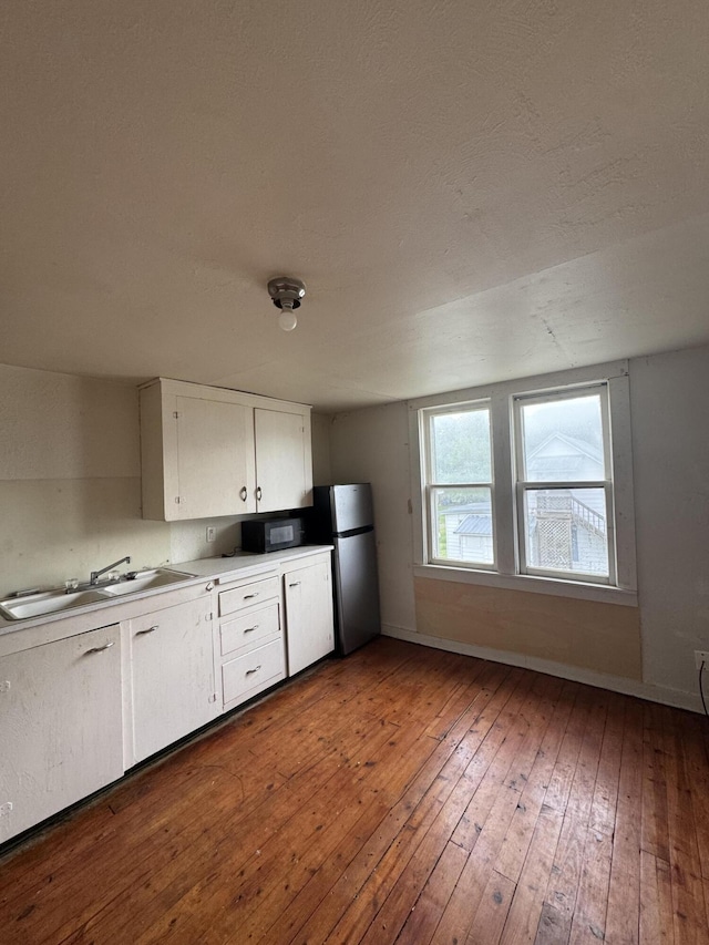 201 W Pennington Ave, Ava, MO 65608 - kitchen featuring freestanding refrigerator, black microwave, hardwood / wood-style flooring, white cabinetry, and light countertops
