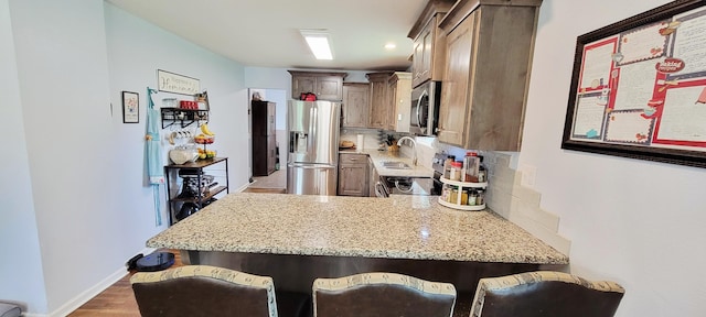524 Niangua Rd, Niangua, MO 65713 - kitchen with appliances with stainless steel finishes, a peninsula, decorative backsplash, light stone countertops, and a kitchen bar