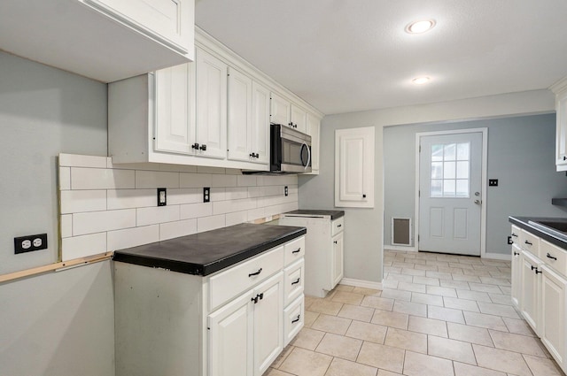 902 S Hickory St, Mount Vernon, MO 65712 - kitchen featuring stainless steel microwave, dark countertops, backsplash, white cabinetry, and recessed lighting