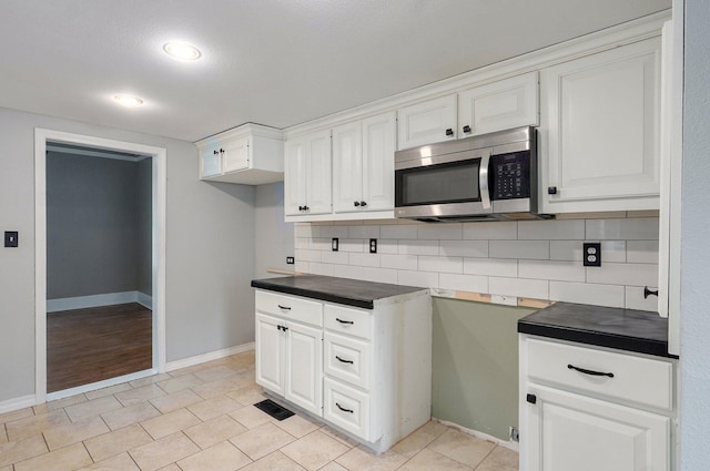 902 S Hickory St, Mount Vernon, MO 65712 - kitchen featuring stainless steel microwave, dark countertops, backsplash, white cabinets, and light tile patterned flooring