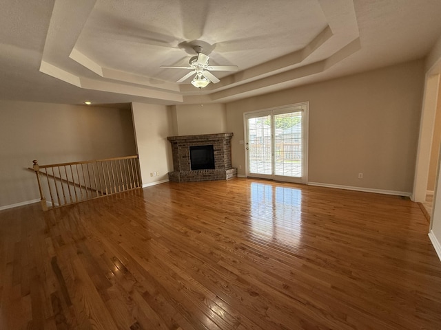 5218 S Gary Ct, Springfield, MO 65810 - unfurnished living room with a tray ceiling, a ceiling fan, wood finished floors, and a brick fireplace