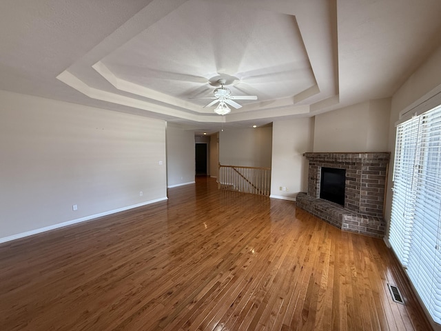 5218 S Gary Ct, Springfield, MO 65810 - unfurnished living room with a raised ceiling, wood finished floors, a ceiling fan, and a brick fireplace