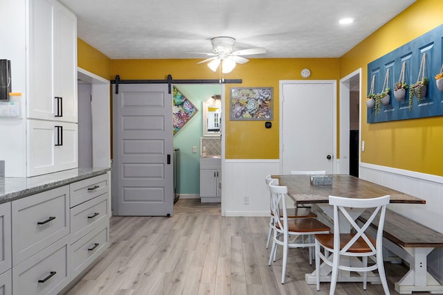 3449 N Rogers Ave, Springfield, MO 65803 - dining area featuring a barn door, a ceiling fan, wainscoting, and light wood-type flooring