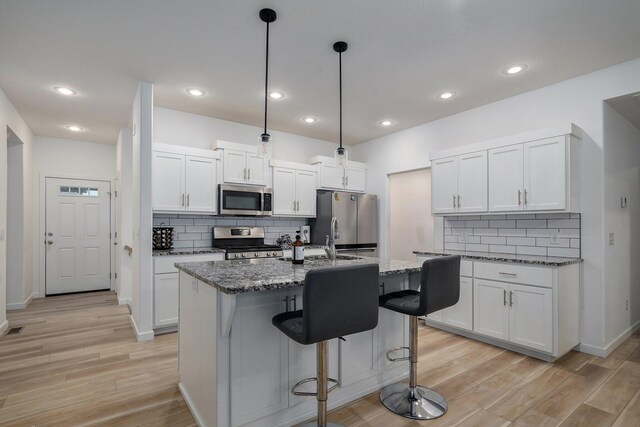 842 E Acacia Ln, Nixa, MO 65714 - kitchen with stainless steel appliances, light wood finished floors, a kitchen breakfast bar, decorative backsplash, and recessed lighting