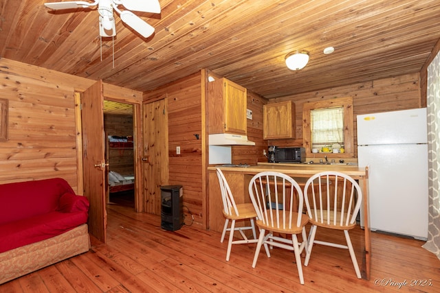 378 63rd Hwy S, Mammoth Spring, AR 72554 - kitchen with freestanding refrigerator, wooden walls, wood-type flooring, a ceiling fan, and a wood stove