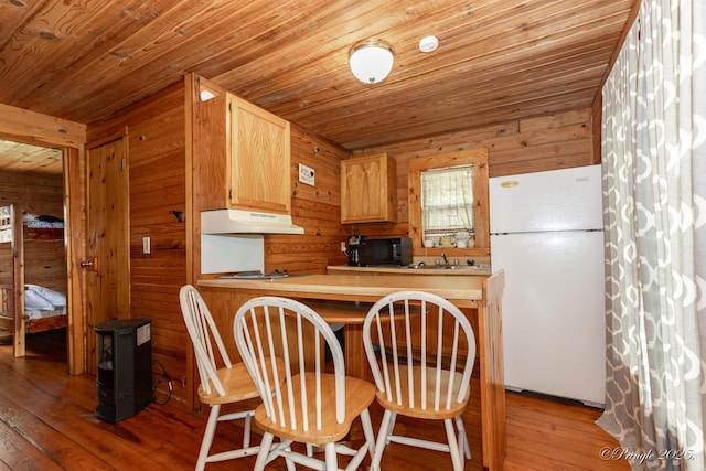 378 63rd Hwy S, Mammoth Spring, AR 72554 - kitchen with freestanding refrigerator, under cabinet range hood, black microwave, wood walls, and hardwood / wood-style flooring