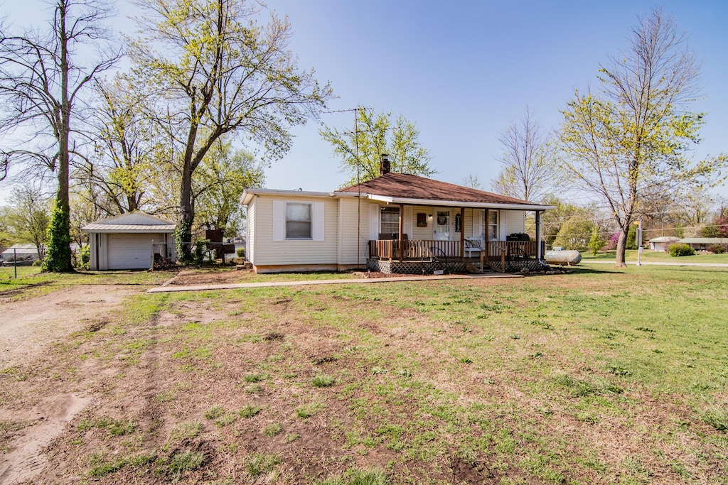 317 W 1st St, Miller, MO 65707 - ranch-style house with a porch, a detached garage, a front yard, a chimney, and dirt driveway
