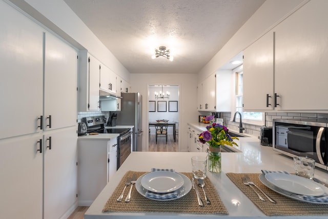 2443 S Kickapoo Ave, Springfield, MO 65804 - kitchen featuring stainless steel appliances, under cabinet range hood, decorative backsplash, a chandelier, and a textured ceiling