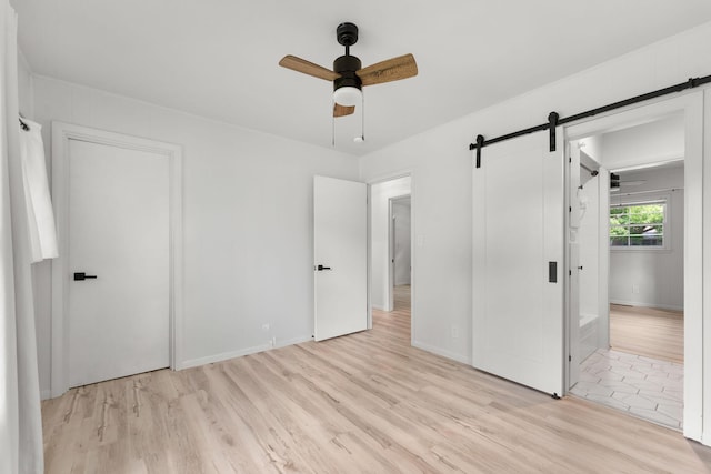 2443 S Kickapoo Ave, Springfield, MO 65804 - unfurnished bedroom featuring a barn door, light wood-style floors, and a ceiling fan