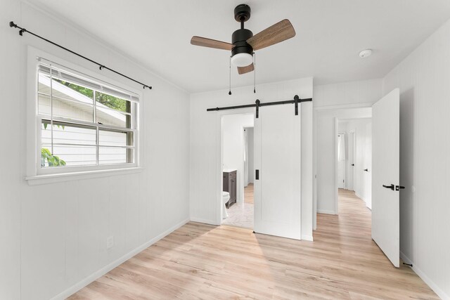 2443 S Kickapoo Ave, Springfield, MO 65804 - unfurnished bedroom with a barn door, light wood-style flooring, and ceiling fan