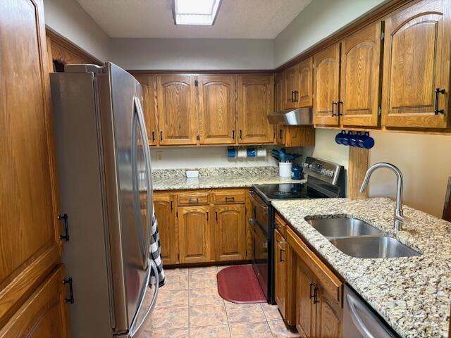 21572 Lawrence Unit 1240, Aurora, MO 65605 - kitchen featuring stainless steel appliances, brown cabinets, under cabinet range hood, light stone counters, and light tile patterned flooring