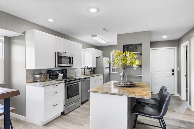 kitchen with appliances with stainless steel finishes, a kitchen island, a breakfast bar, white cabinets, and backsplash