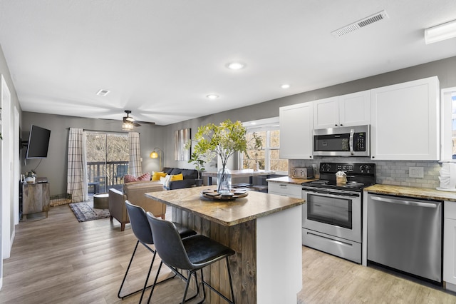 kitchen featuring stainless steel appliances, a kitchen breakfast bar, white cabinetry, light wood-style floors, and recessed lighting