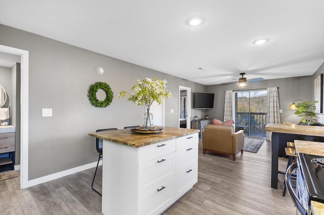 kitchen featuring a ceiling fan, white cabinets, a breakfast bar area, range, and light wood finished floors