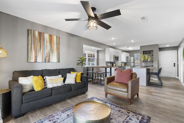 living area with healthy amount of natural light, light wood-style floors, a ceiling fan, and recessed lighting
