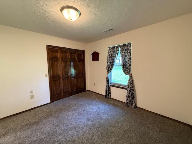 2604 Country Dr, Mountain Grove, MO 65711 - unfurnished bedroom featuring a textured ceiling, dark colored carpet, and a closet