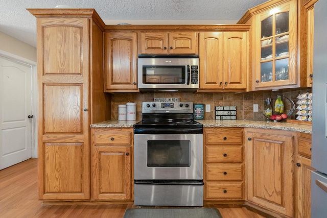 3223 W Melbourne St, Springfield, MO 65810 - kitchen featuring appliances with stainless steel finishes, a textured ceiling, light wood-style floors, glass insert cabinets, and decorative backsplash