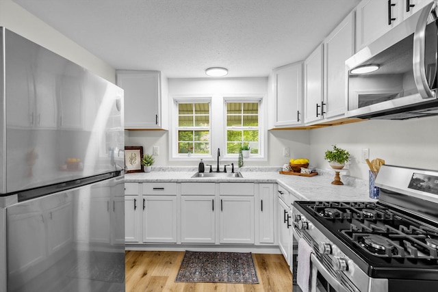 1024 N Fulbright Ave, Springfield, MO 65802 - kitchen with appliances with stainless steel finishes, white cabinetry, light wood-type flooring, a textured ceiling, and light stone counters