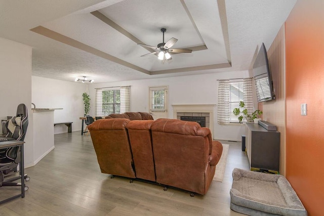 828 S Chinkapin Ave, Nixa, MO 65714 - living area featuring ceiling fan, a tray ceiling, light wood-style floors, a tiled fireplace, and a textured ceiling