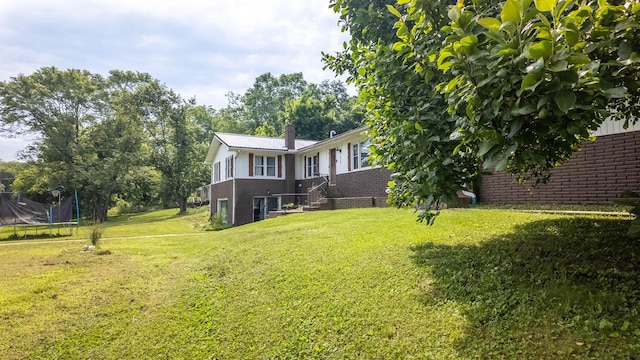 1160 Bethel Ave, Mammoth Spring, AR 72554 - rear view of property featuring brick siding, a trampoline, a chimney, and a lawn