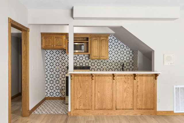 2661 E Ridgewood Dr, Springfield, MO 65804 - kitchen featuring stainless steel microwave, light countertops, tasteful backsplash, a kitchen bar, and brown cabinets