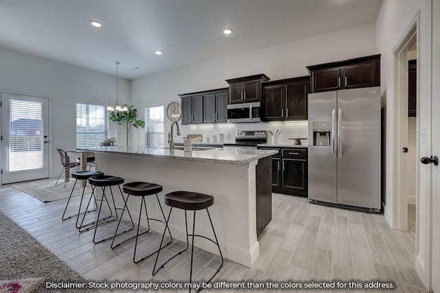 703 N Baywood Dr, Nixa, MO 65714 - kitchen featuring appliances with stainless steel finishes, light wood finished floors, a breakfast bar, a kitchen island with sink, and recessed lighting