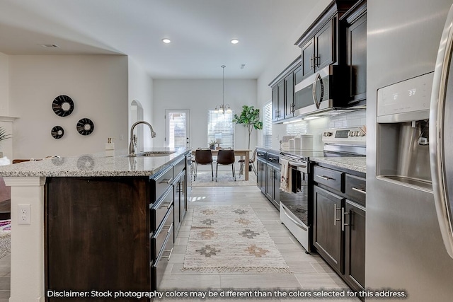 703 N Baywood Dr, Nixa, MO 65714 - kitchen with stainless steel appliances, recessed lighting, an island with sink, light stone counters, and dark brown cabinetry