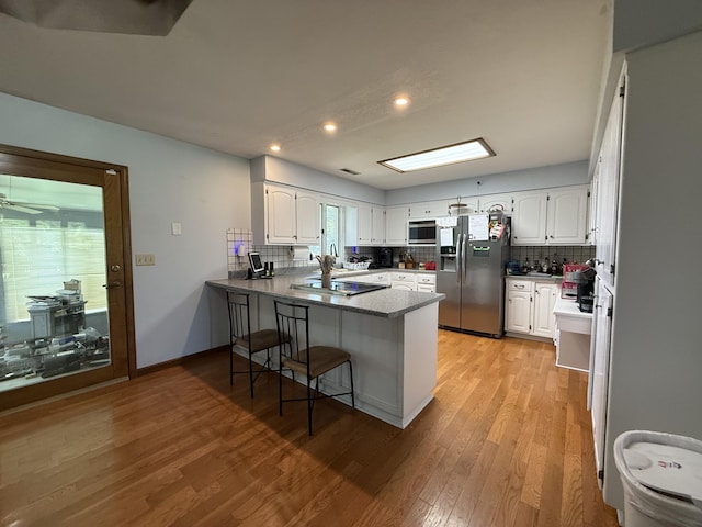 1301 W Blair Dr, Stockton, MO 65785 - kitchen featuring appliances with stainless steel finishes, a peninsula, light wood-type flooring, decorative backsplash, and white cabinetry