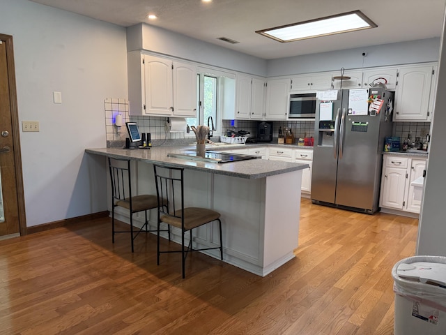 1301 W Blair Dr, Stockton, MO 65785 - kitchen with appliances with stainless steel finishes, a peninsula, tasteful backsplash, white cabinets, and light wood-style flooring
