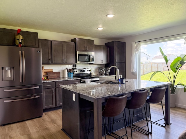 404 N Pine Leaf Rd, Nixa, MO 65714 - kitchen with stainless steel appliances, a textured ceiling, a kitchen bar, an island with sink, and decorative backsplash