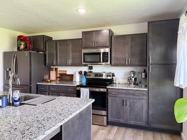 404 N Pine Leaf Rd, Nixa, MO 65714 - kitchen featuring appliances with stainless steel finishes, dark brown cabinets, light wood-type flooring, a textured ceiling, and decorative backsplash