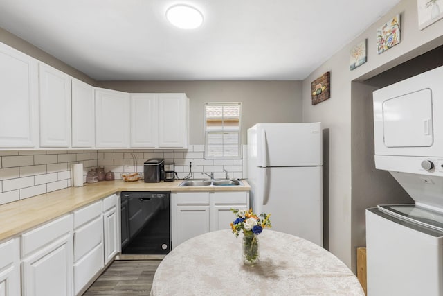 2116 N Main Ave, Springfield, MO 65803 - kitchen featuring black dishwasher, freestanding refrigerator, stacked washer / dryer, decorative backsplash, and white cabinets