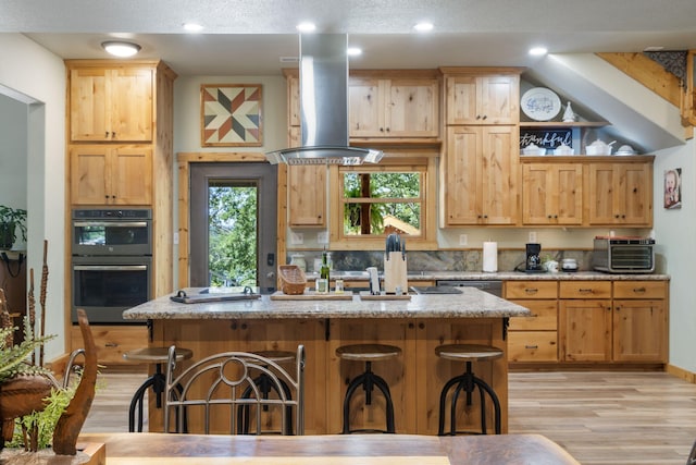 26474 Kings River Rd, Shell Knob, MO 65747 - kitchen featuring wall chimney range hood, stainless steel double oven, light wood-style flooring, a kitchen breakfast bar, and a center island