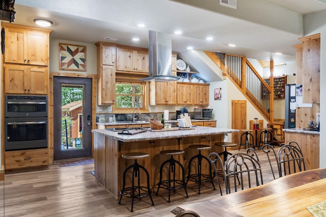 26474 Kings River Rd, Shell Knob, MO 65747 - kitchen with island range hood, a breakfast bar area, a kitchen island, wood finished floors, and light stone counters