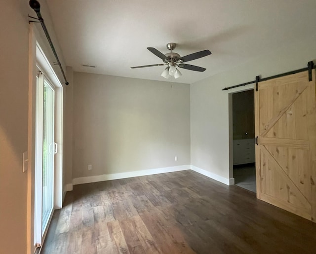 24136 Lazy Daze Ln, Wheatland, MO 65779 - unfurnished bedroom with a barn door, dark wood-style floors, ensuite bath, and ceiling fan
