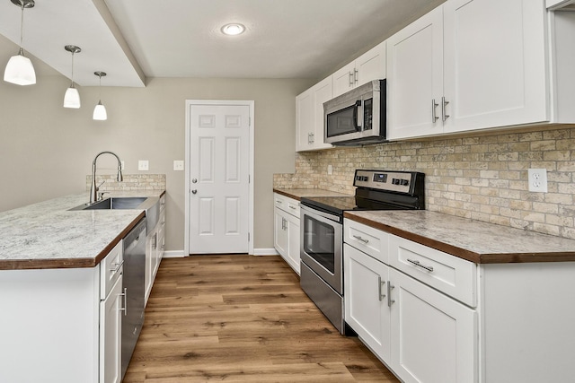 3539 S Walnut Hill Dr, Springfield, MO 65807 - kitchen featuring appliances with stainless steel finishes, a peninsula, backsplash, light wood-style flooring, and white cabinets