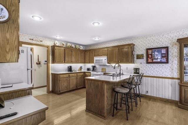 3416 S Barnes Ave, Springfield, MO 65804 - kitchen with white appliances, wallpapered walls, a peninsula, light wood-style flooring, and a kitchen breakfast bar