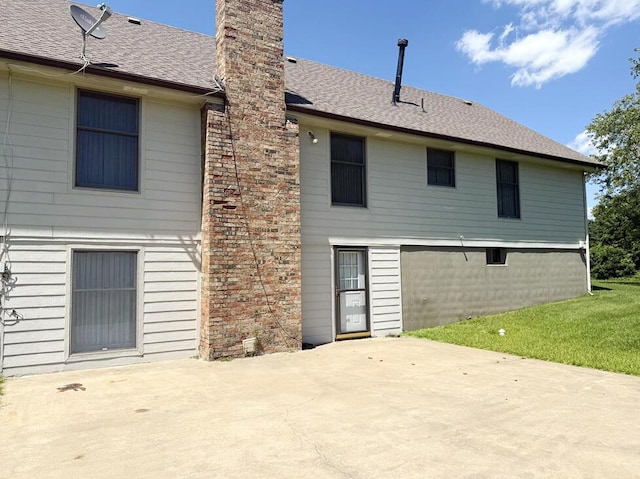 114 W Carman Rd, El Dorado Springs, MO 64744 - rear view of property featuring a patio, a chimney, roof with shingles, and a lawn