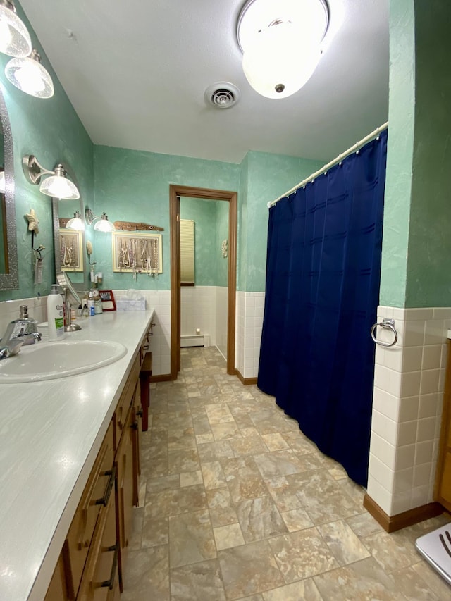 1605 S Park Ave, Aurora, MO 65605 - bathroom with tile walls, vanity, baseboard heating, a wainscoted wall, and stone finish flooring