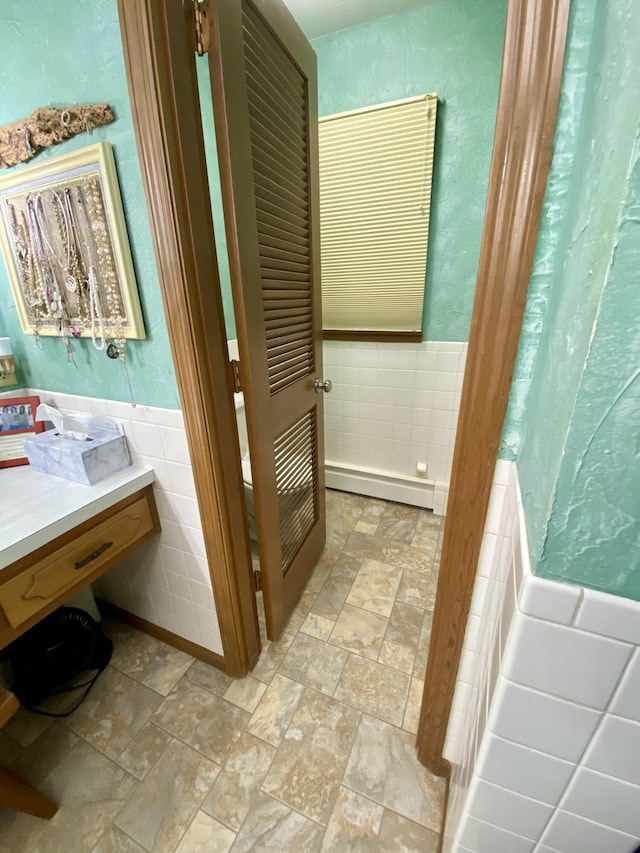 1605 S Park Ave, Aurora, MO 65605 - full bathroom with baseboard heating, tile walls, vanity, stone finish flooring, and wainscoting