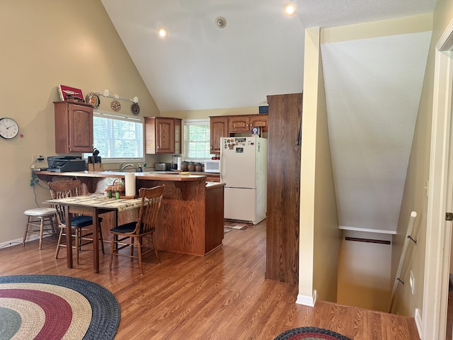 26569 County Road 225, Flemington, MO 65650 - kitchen with white appliances, a peninsula, light wood-type flooring, a kitchen bar, and brown cabinets