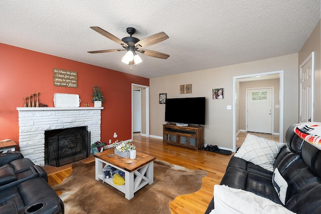 1704 E Latoka St, Springfield, MO 65804 - living room featuring a ceiling fan, wood finished floors, a stone fireplace, and a textured ceiling