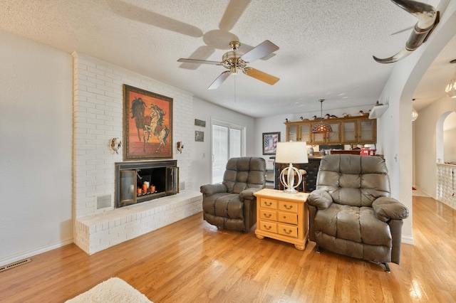 29 Trail Ridge Dr, Kimberling City, MO 65686 - living area with arched walkways, a textured ceiling, light wood-type flooring, a brick fireplace, and a ceiling fan