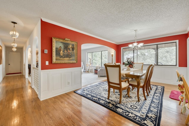 29 Trail Ridge Dr, Kimberling City, MO 65686 - dining room with arched walkways, a chandelier, a textured ceiling, light wood-style flooring, and wainscoting