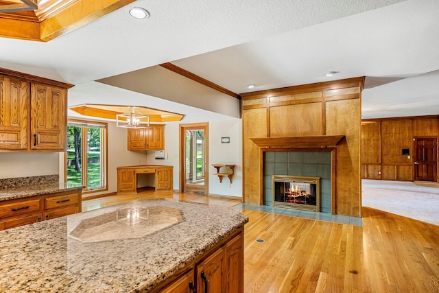 2347 E Nottingham St, Springfield, MO 65804 - kitchen featuring open floor plan, light wood finished floors, light stone countertops, a tile fireplace, and brown cabinets