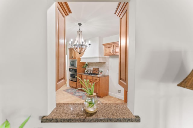 1303 E Eaglegate Pkwy, Springfield, MO 65804 - kitchen featuring appliances with stainless steel finishes, a chandelier, backsplash, light wood-style floors, and premium range hood