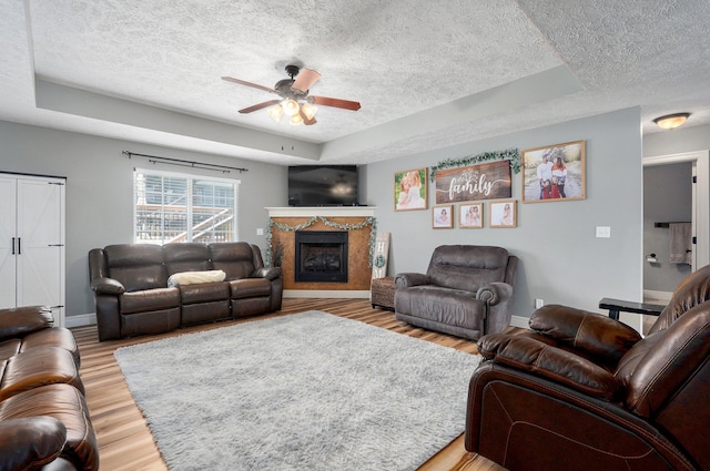 4531 W Somerset Dr, Battlefield, MO 65619 - living room with a textured ceiling, a raised ceiling, a ceiling fan, a fireplace, and light wood-type flooring