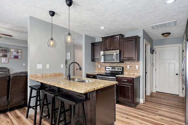 4531 W Somerset Dr, Battlefield, MO 65619 - kitchen with appliances with stainless steel finishes, dark brown cabinetry, light wood-style flooring, a kitchen bar, and tasteful backsplash